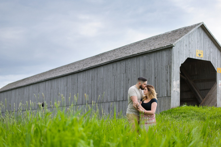 Couple in field with covered bridge