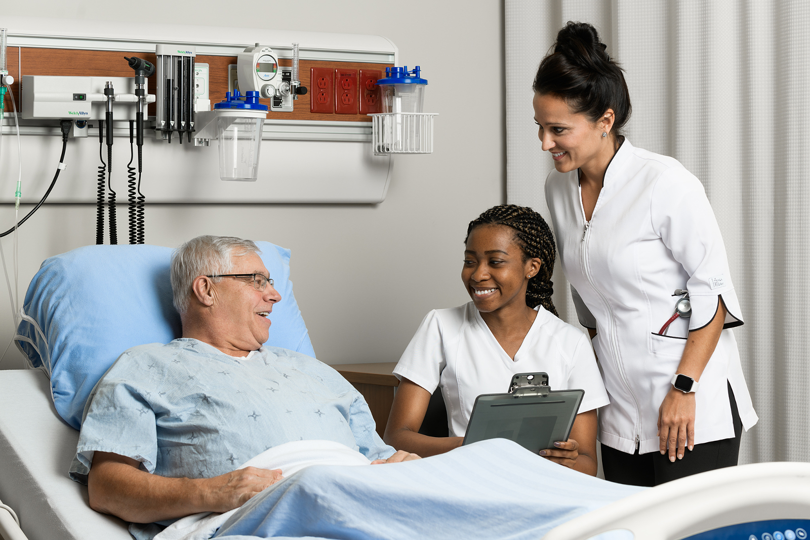 Male patient laying in hospital bed with two female nurses assessing